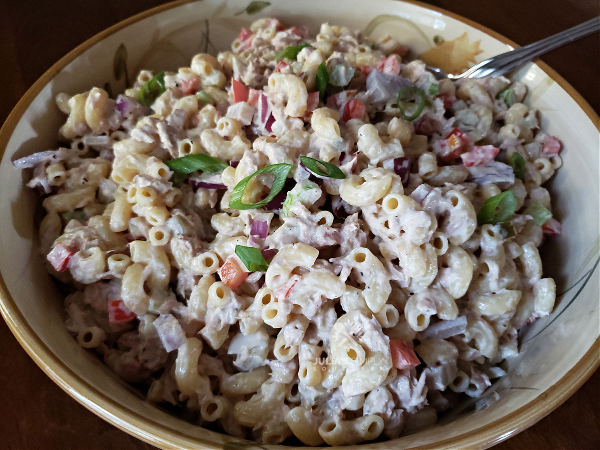 A large serving bowl with creamy tuna macaroni salad garnished with scallions