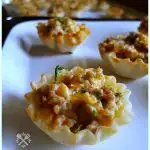 Spicy Sausage Tarts in Phyllo mini cups on a white platter for a Christmas and New Year party