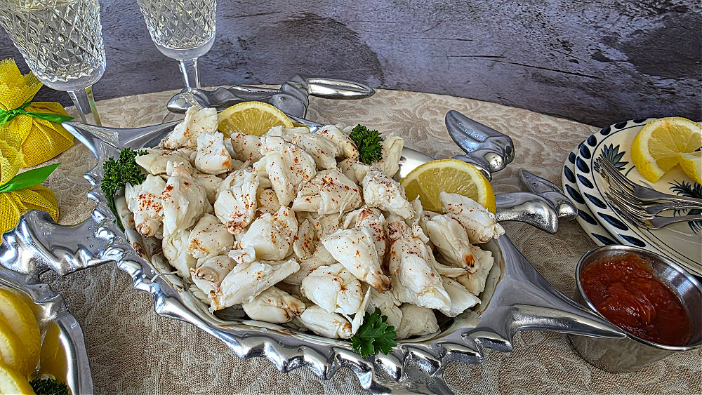 A beautiful display of an elegant crab cocktail in a silver serving dish with offerings of cocktail sauce and lemon edges