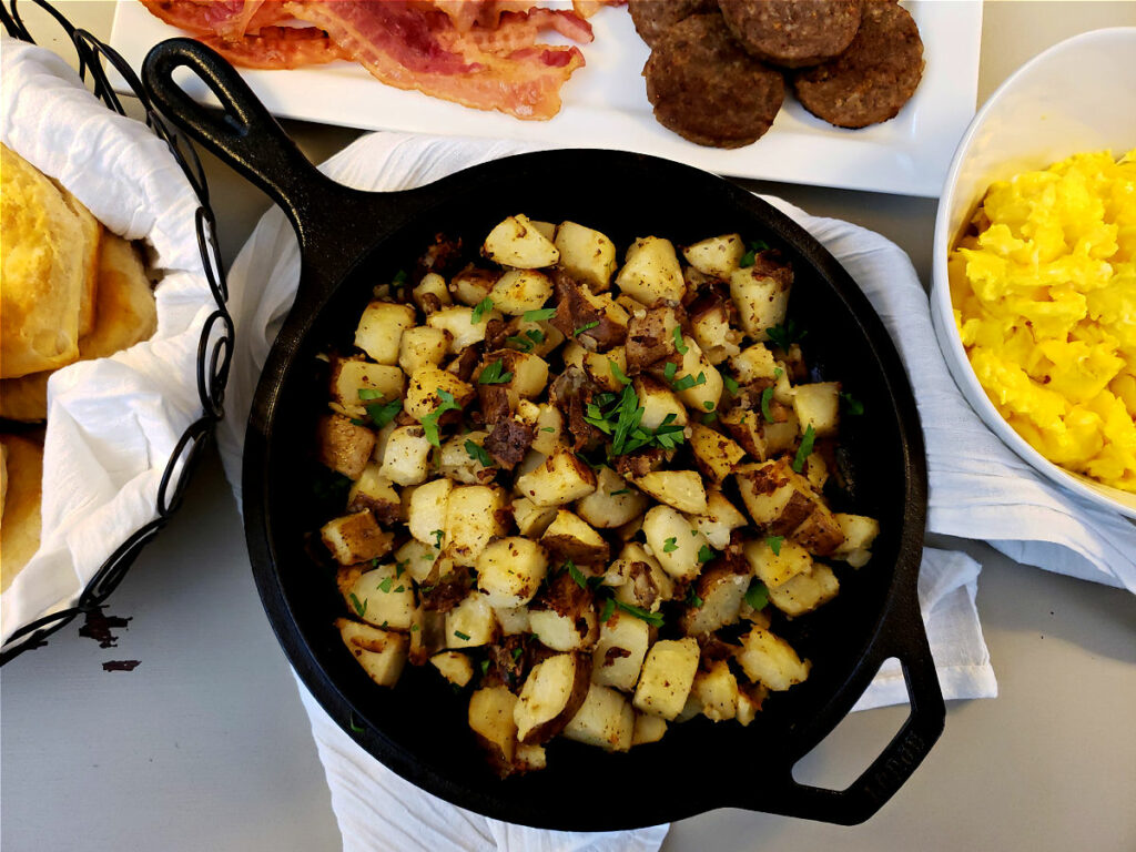 Breakfast potatoes in a cast iron skillet served with biscuits, bacon, sausage, and eggs