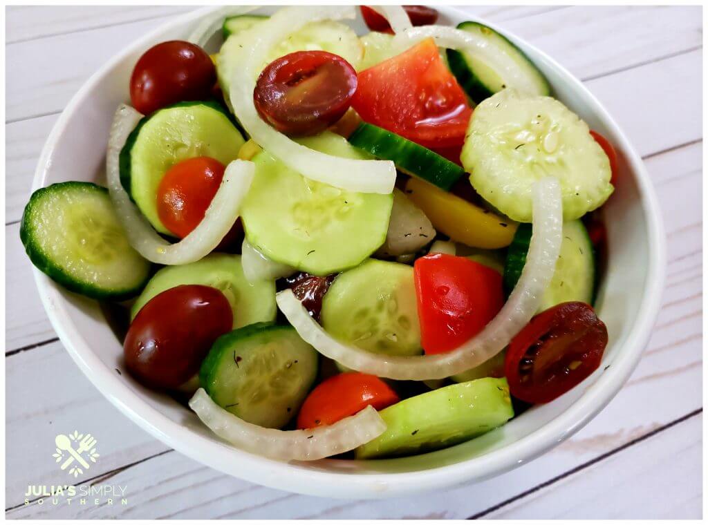 Colorful cucumber salad with tomatoes and onions in a white serving bowl