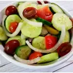 Colorful cucumber salad with tomatoes and onions in a white serving bowl