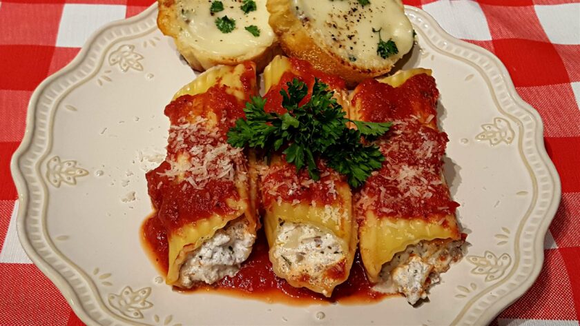 Beef manicotti with red sauce on a plate with a side of garlic cheese toast