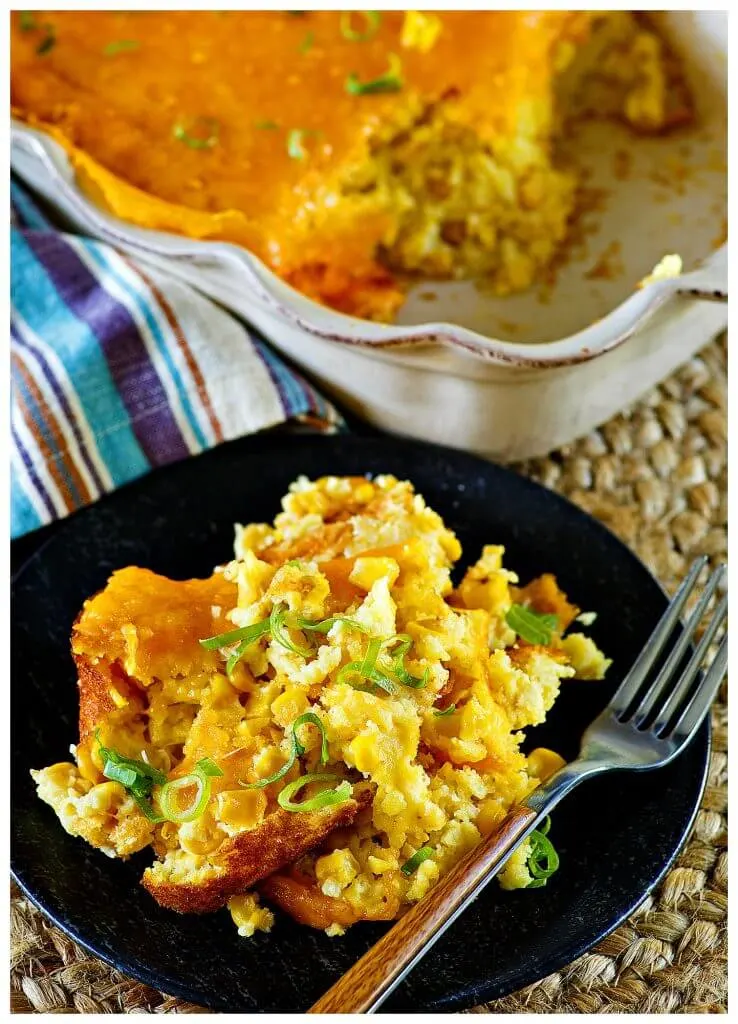 Delicious serving of a corn pudding souffle on a black plate with a form topped with scallions