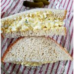 Simple egg salad sandwich recipe on a glass plate on top of a red and white ticking towel