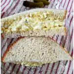 Simple egg salad sandwich recipe on a glass plate on top of a red and white ticking towel