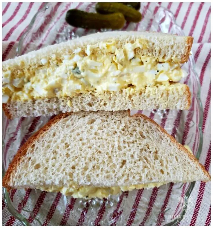 Simple egg salad sandwich recipe on a glass plate on top of a red and white ticking towel