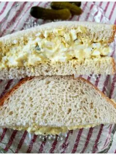 Simple egg salad sandwich recipe on a glass plate on top of a red and white ticking towel