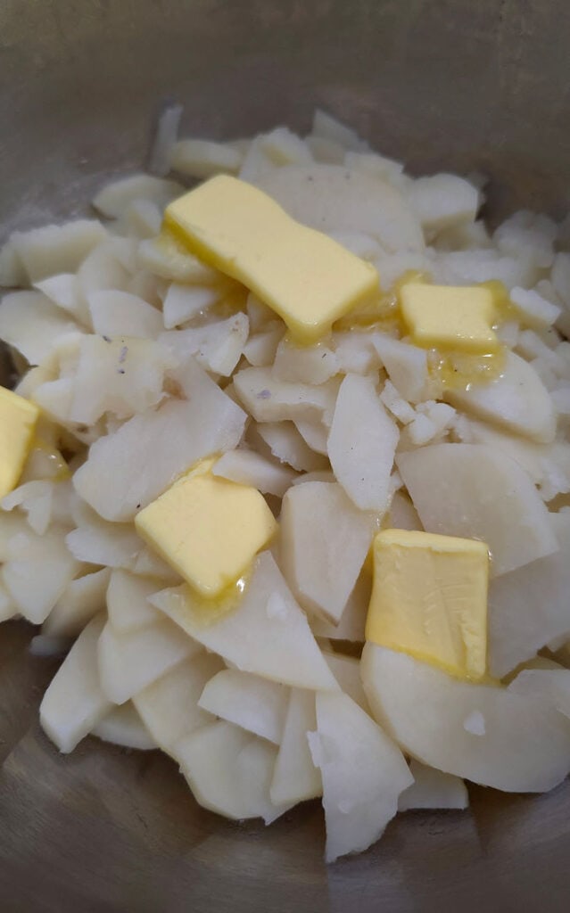 Adding butter to drained boiled potatoes before mashing