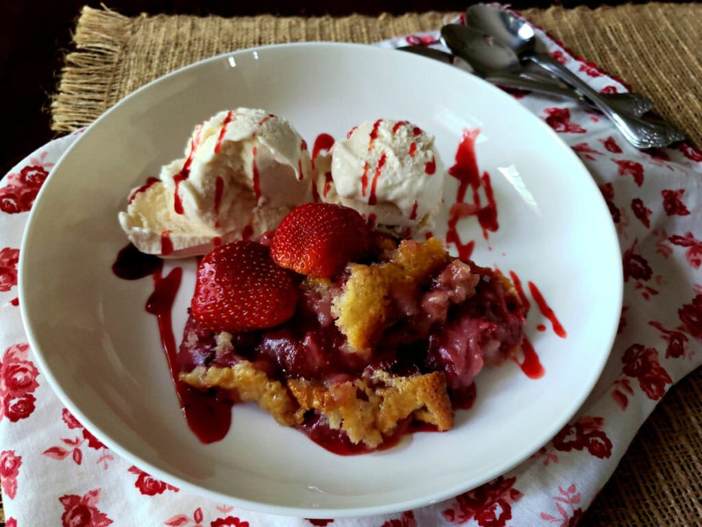 Easy strawberry cobbler recipe served in a white bowl with vanilla ice cream and drizzled strawberry sundae syrup