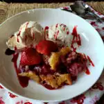 Easy strawberry cobbler recipe served in a white bowl with vanilla ice cream and drizzled strawberry sundae syrup