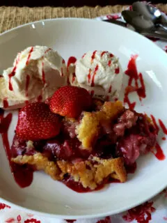 Easy strawberry cobbler recipe served in a white bowl with vanilla ice cream and drizzled strawberry sundae syrup