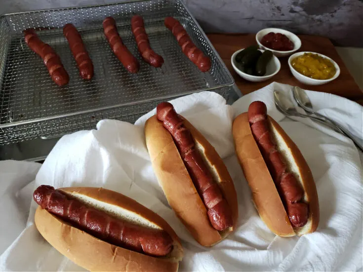hot dog buns with crispy hot dogs cooked in an air fryer with topping options on a white tablecloth