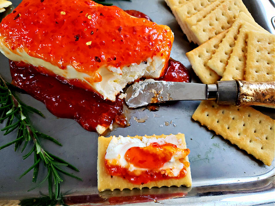 serving tray with a block of cream cheese topped with pepper jelly served with club crackers