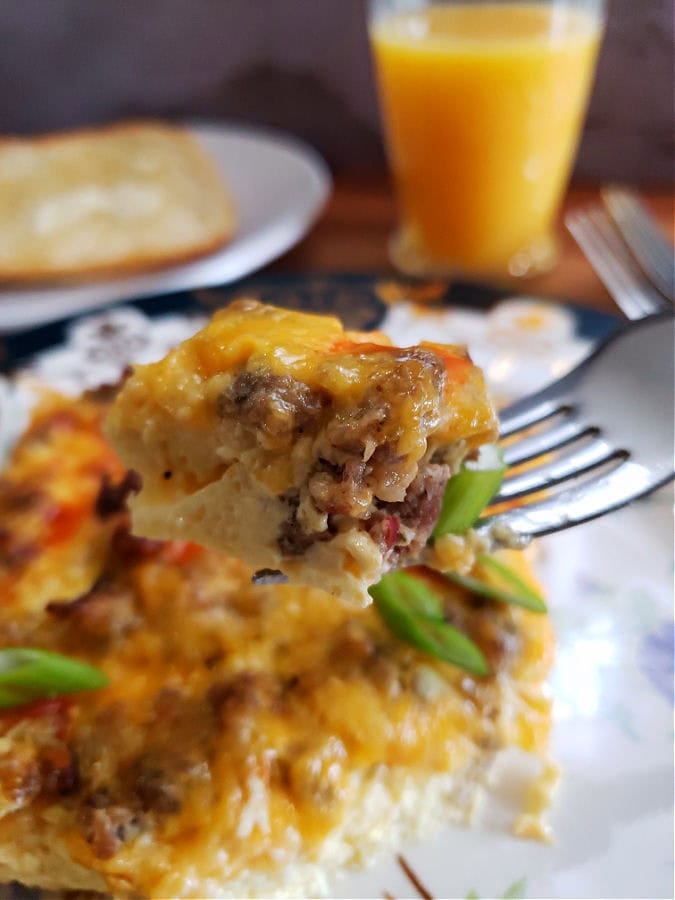 A make ahead breakfast casserole serving with a delicious bite on a fork highlighting the egg, sausage, and cheese