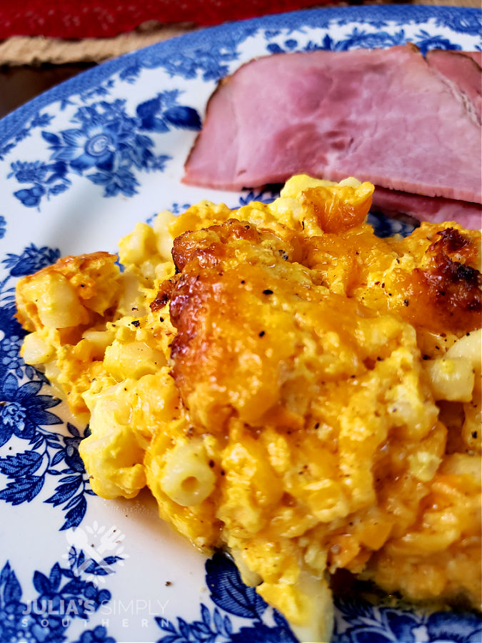 Crock Pot Macaroni and Cheese served on a blue and white floral plate with sliced baked ham