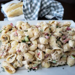 Serving platter with salmon pasta salad with mayo lemon dill and caper dressing served with bread baguettes