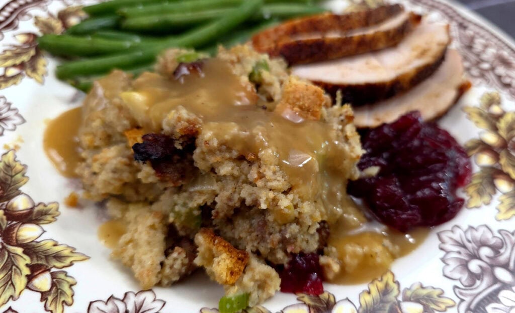 a Thanksgiving pattern plate with cornbread dressing with sausage, apple, and sage served with cranberry, turkey and green beans