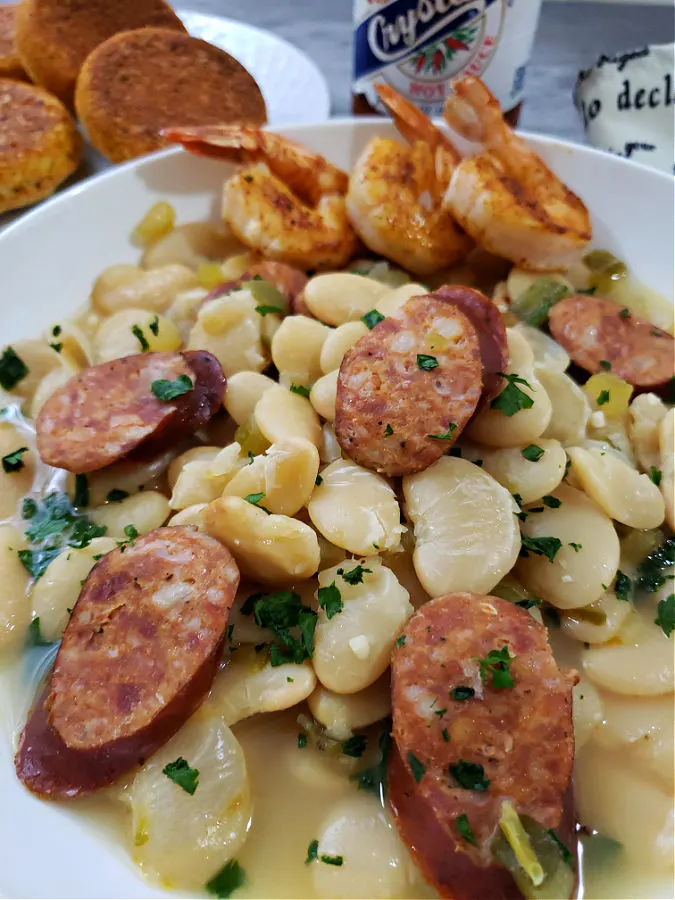 A white bowl of creamy butter beans with shrimp and sausage served with cornbread