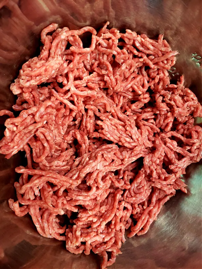 loosening ground beef into stainless mixing bowl to prepare meatballs