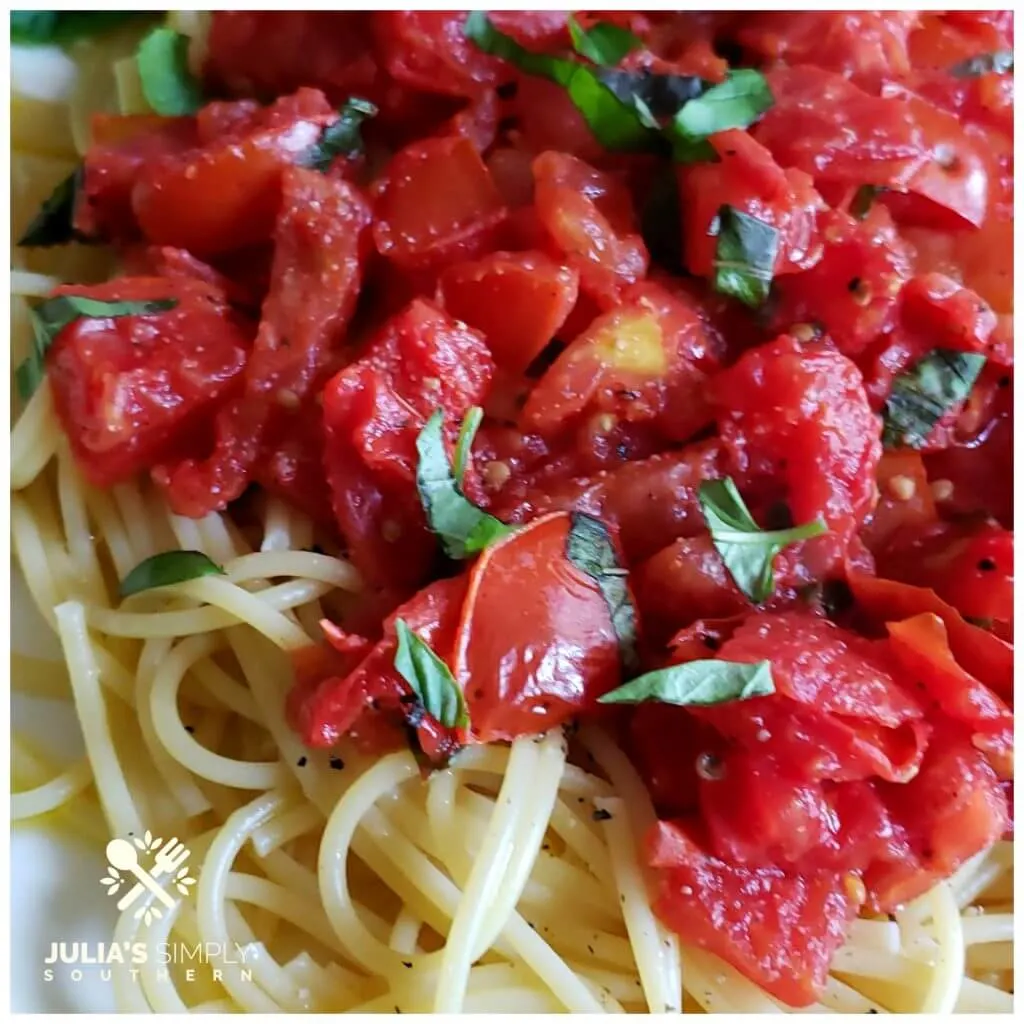 Beautiful red stewed Roma tomatoes on a bed of pasta with fresh basil and olive oil