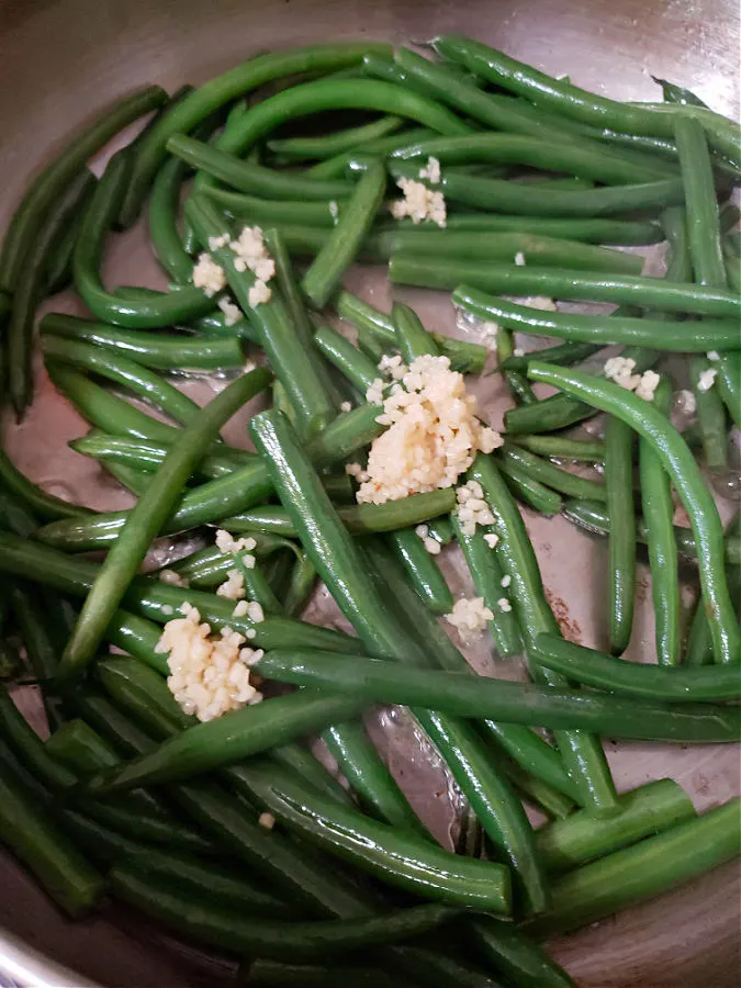 Sautéing green beans with minced garlic.
