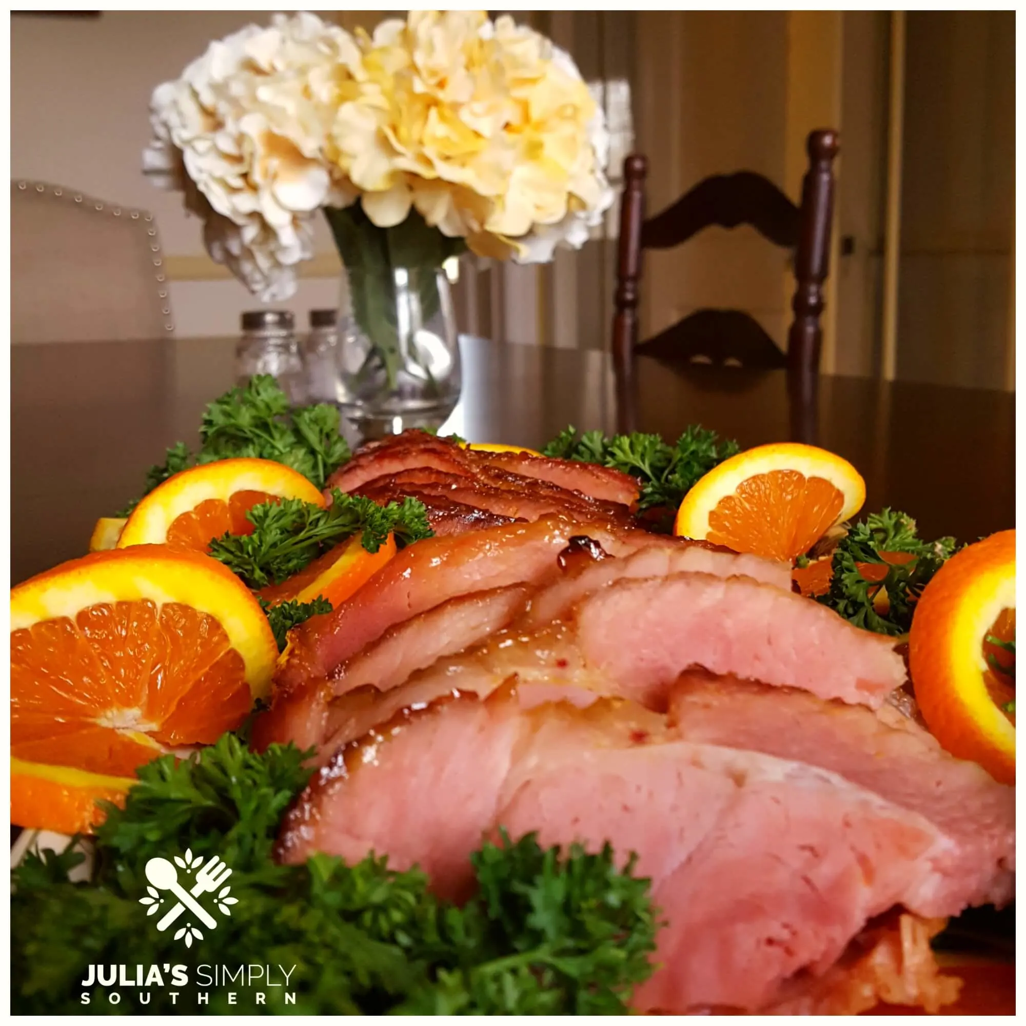Glazed Ham with a Honey Orange Glaze on a dining table with flowers in the background.