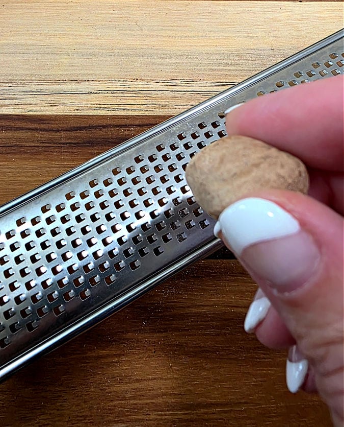whole nutmeg being grated on a micro plane grater to add to a holiday cookie recipe
