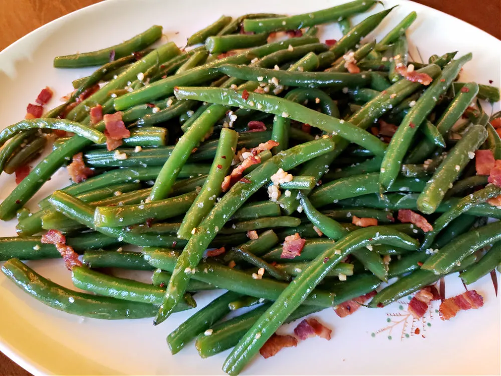 Sautéed Fresh Green Beans with Garlic and Bacon on a serving plate with a pinch of red pepper flakes.