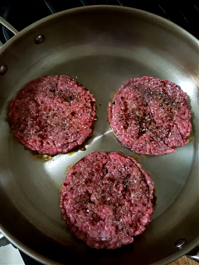 Seasoned beef patties in a stainless skillet