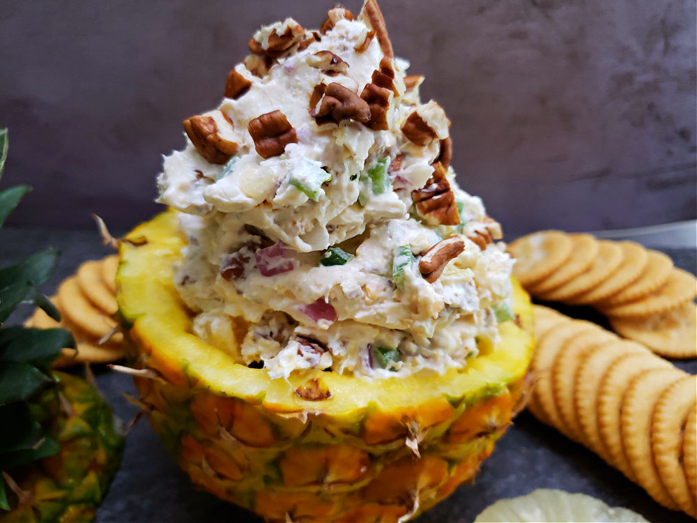 a hollow pineapple half filled with pineapple cheese ball spread being served with crackers for a delicious party appetizer