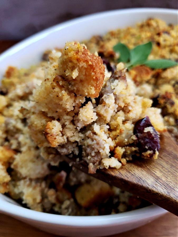 wooden spoon serving out cornbread dressing from a white oval baking dish