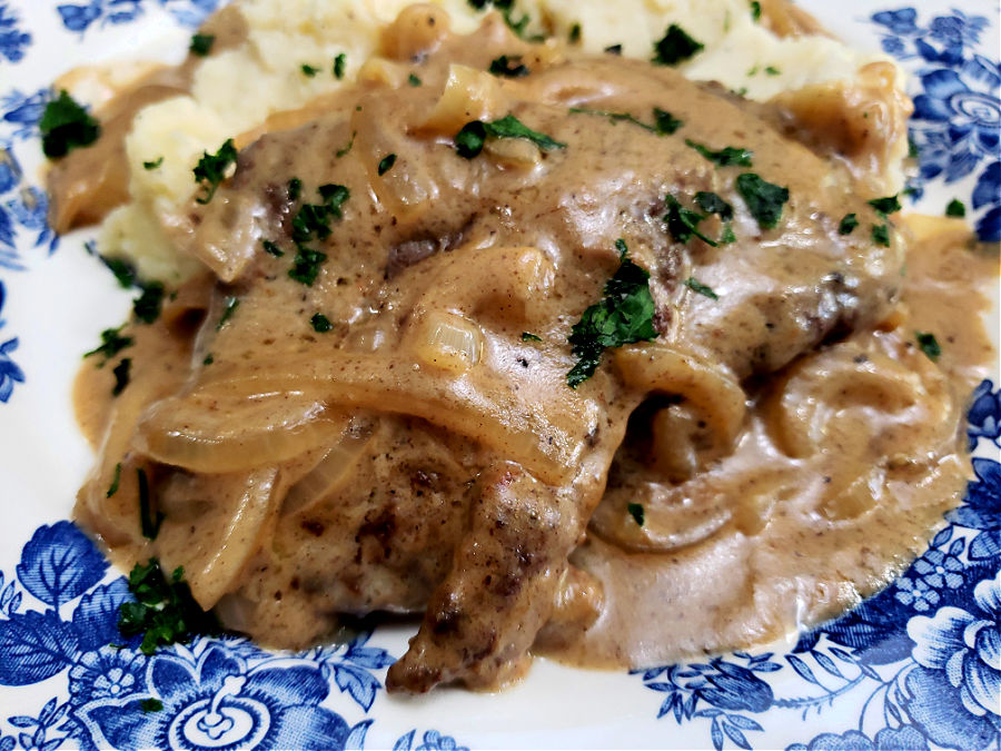 A blue and white place with a bed of mashed potatoes topped with liver, onions and gravy then garnished with parsley