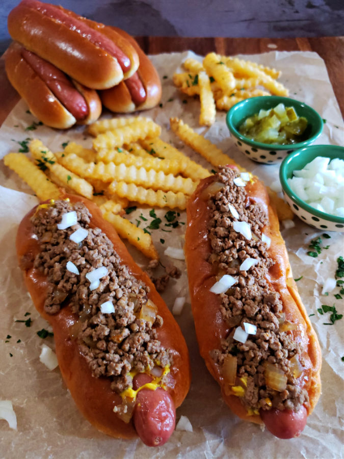 Southern hot dog chili on a couple of hot dogs with brioche buns, fries, pickles and diced onion