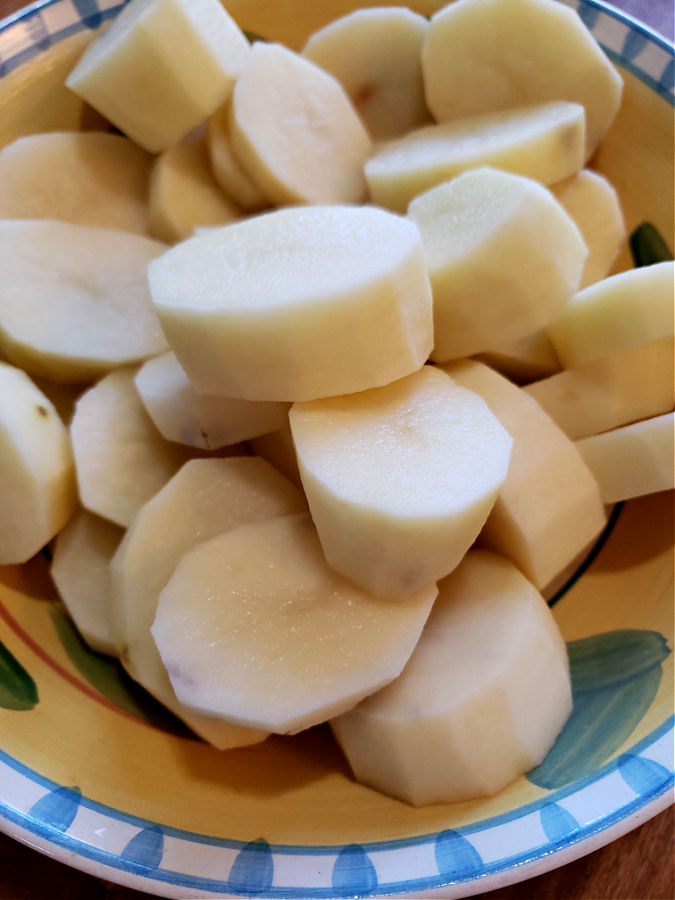 Peeling and cut russet potatoes in a bowl to make roast potatoes in oven