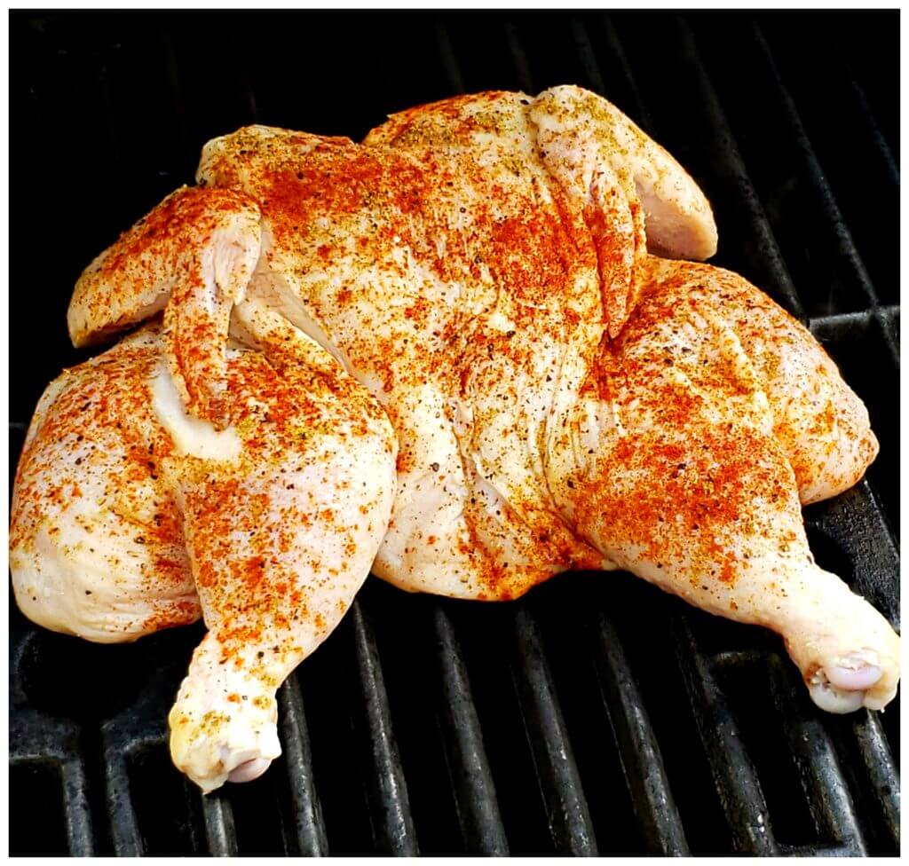 Seasoned whole chicken butterflied and cooking on a gas grill