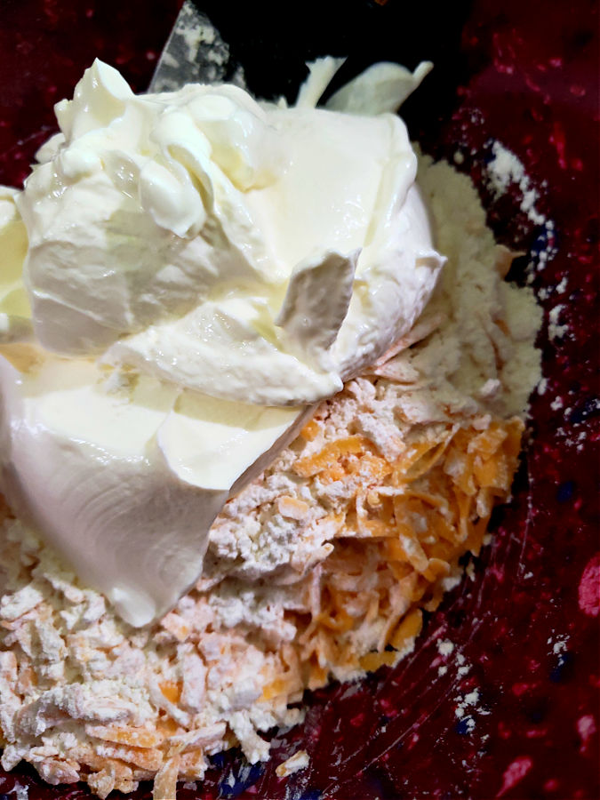 Combining the cheese and flour with organic sour cream in a red mixing bowl