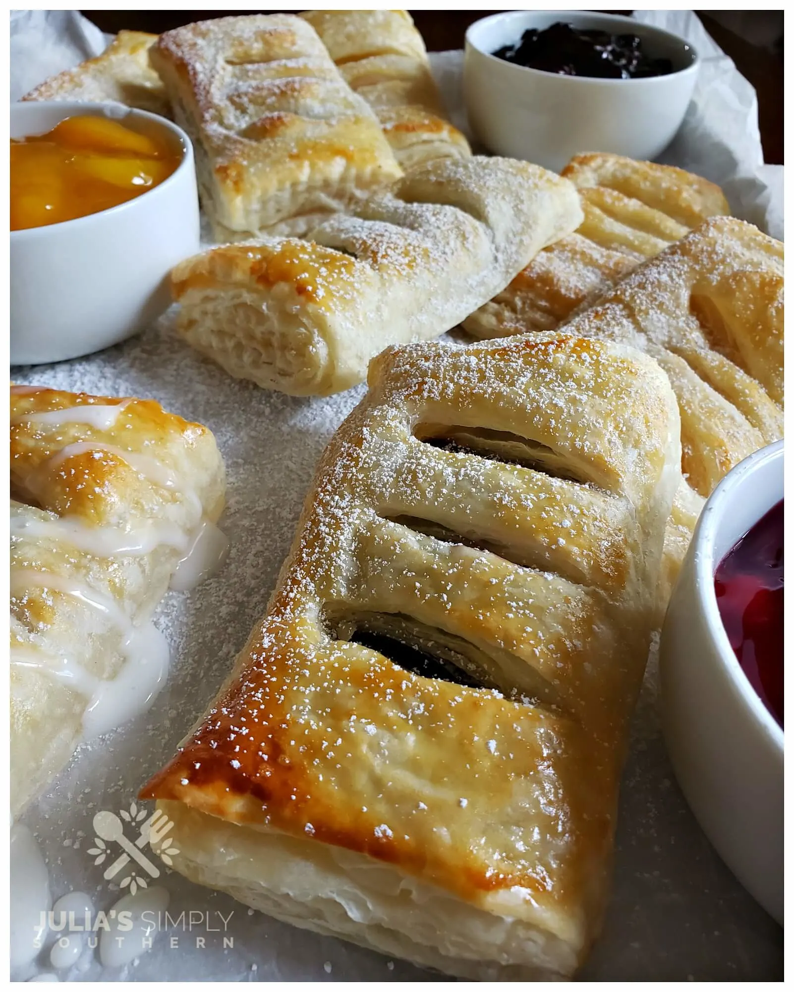 Assorted fruit hand pies on a silver baking sheet that has been lined with parchment paper and dusted with powdered sugar.