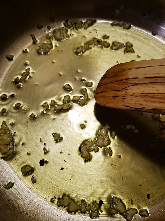 Skillet with olive oil being infused with red pepper flakes and fresh garlic