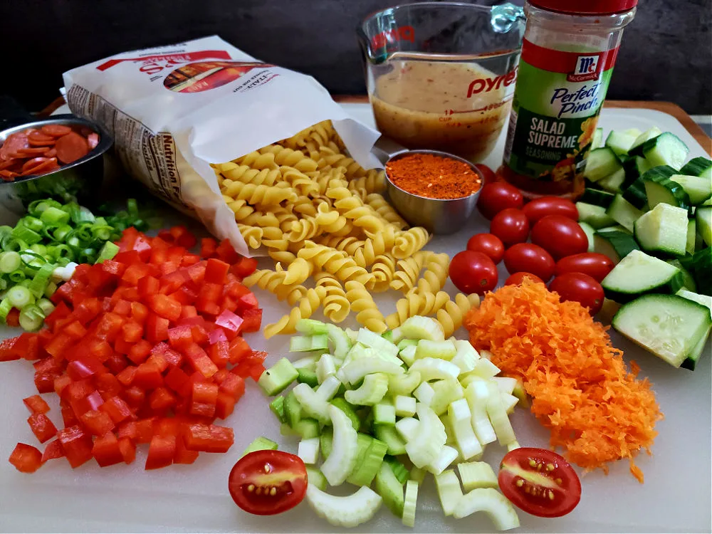 Cutting board with the ingredients needed to prepare a Pasta Salad Recipe with Italian Dressing and Salad Supreme Seasoning