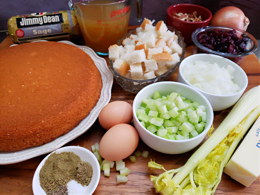 cutting board arranged with the ingredients needed to prepare a holiday cornbread stuffing with sausage, cranberries, and pecans along with the traditional seasonings and aromatics