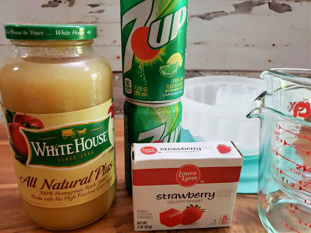 Ingredients for preparing an applesauce congealed salad: jar of applesauce, strawberry gelatin and 7UP