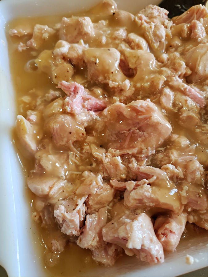 A jar of turkey gravy poured over turkey meat for a casserole meal
