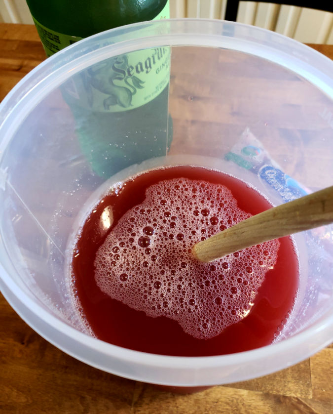 Combining punch drink in a large pitcher stirring with a wooden spoon