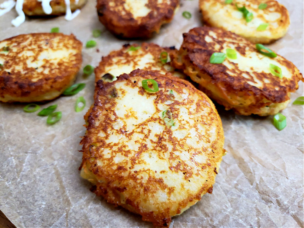 fried mashed potato cakes garnished with green onions on a parchment paper lined serving plate