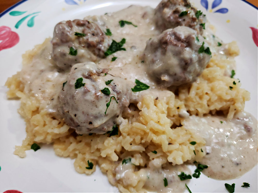 a vintage floral plate with cooked rice topped with creamy meatballs and parsley