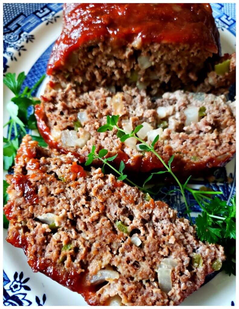 Platter with a glazed meatloaf sliced and garnished with fresh herbs