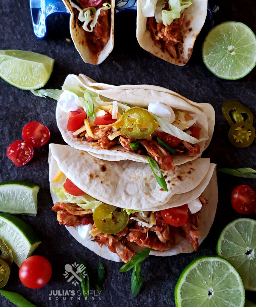 Amazing family meal easy crock pot chicken tacos recipe with toppings surrounded by lime slices and tomatoes
