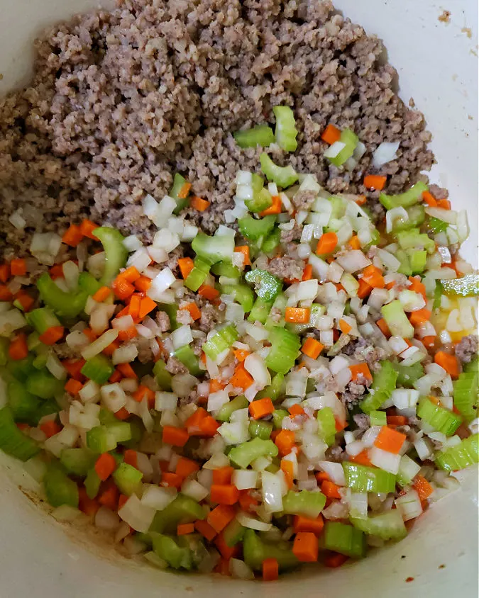 adding aromatic vegetables to the soup pot with browned cooked sausage