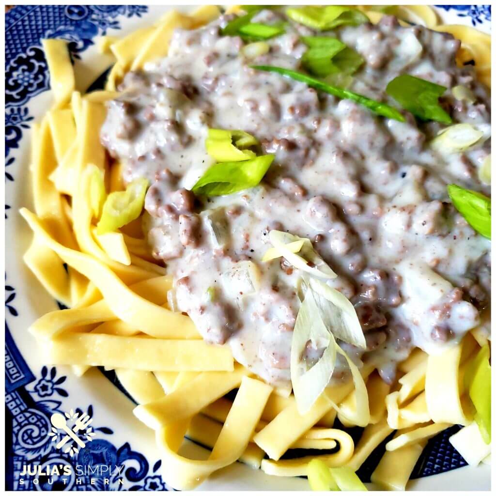 Photo of old fashioned buttered noodles topped with hamburger beef gravy and garnished with scallions on a blue and white plate